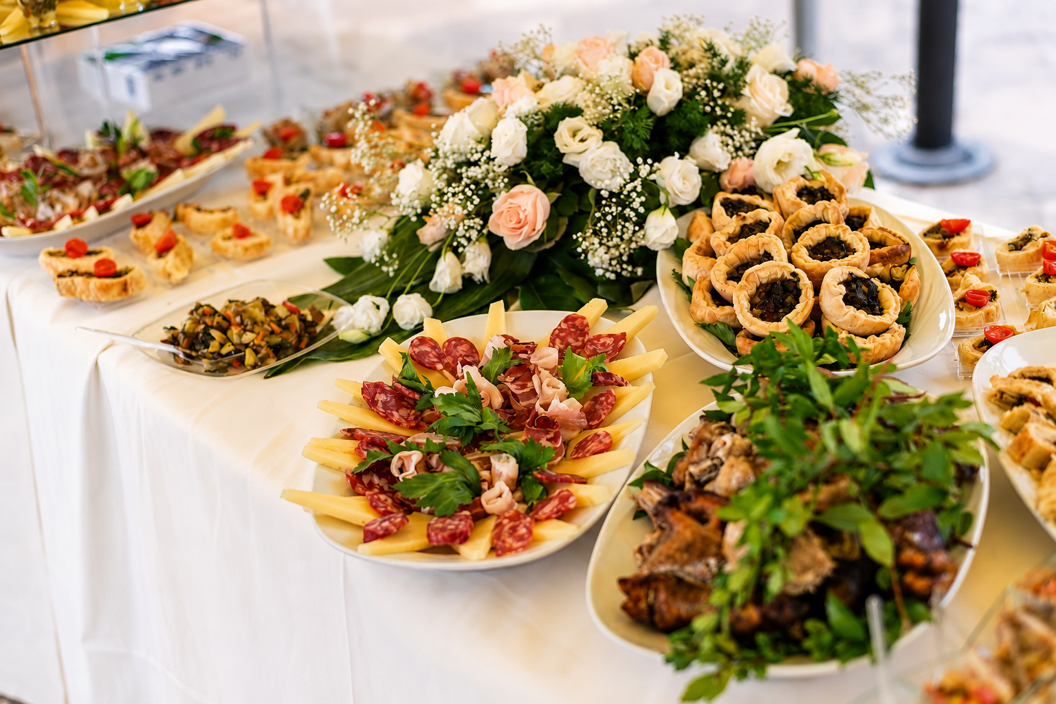 A catered event table with charcuterie, pastries, flowers, and appetizers